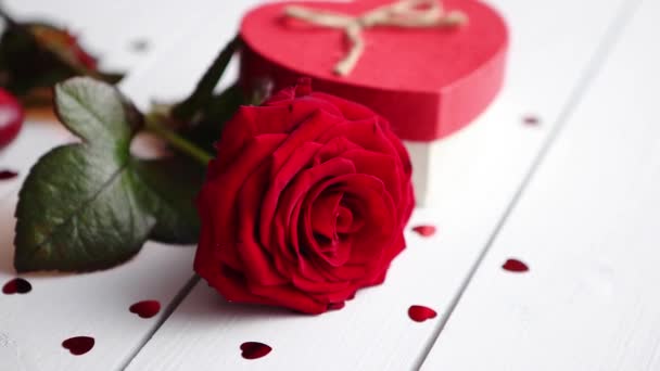 单朵新鲜的红玫瑰花洒在白色木桌上 上面洒满了心形亮片 盒子里有蜡烛和礼物 情人节或爱情的概念 具有复制空间 — 图库视频影像