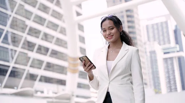 在泰国曼谷的街道上手持和使用手机的亚洲行政工作妇女 其背景是办公楼 图库图片