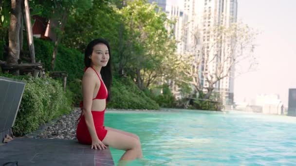 アジアの女性を笑顔でビキニで豪華なプール 木に囲まれて — ストック動画