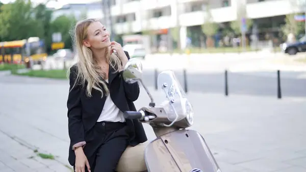 Elegant woman in business attire takes a break on a motor scooter, enjoying a moment of leisure in the city.