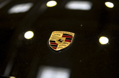 Siyah bir arabanın kaputundaki Porsche ambleminin ayrıntıları.