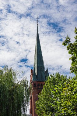 Yeşil yapraklı ağaçların arasında gotik kilise kulesi
