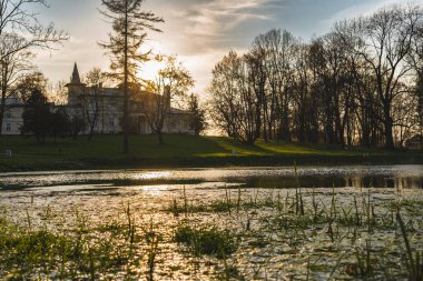 Gün batımında gölün kıyısındaki çimenli bir tepede eski bir malikane.