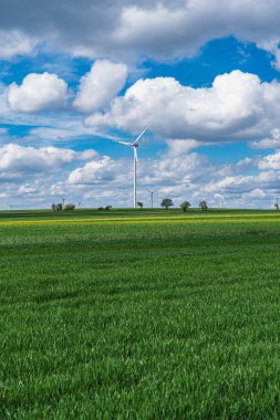Kümülüs bulutlu bahar aylarında tarlada güç türbinleri olan bir rüzgar çiftliğinin manzarası.