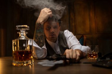 Kollarında dövmeleri olan, beyaz gömlekli, tüvit yelekli ve düz şapkalı İngiliz gangsterler gibi görünen hafif sarhoş bir adam masada oturmuş, elinde bir sürahi viski, tüttürüyor ve tabanca tutuyordu.