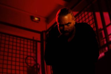 Portrait of bearded man standing with cigar in mouth outdoors at night, looking defiantly at camera