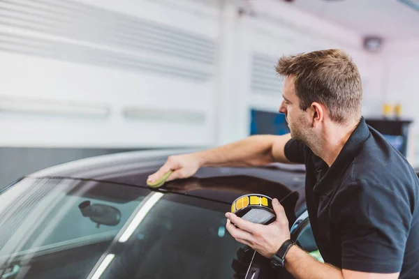 Service man applying wax or coating on car in detailing workshop. Professional work