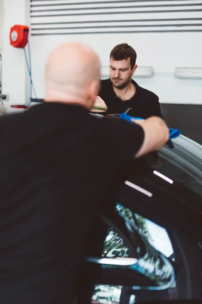 Service men applying wax or coating on car in detailing workshop. Professional work