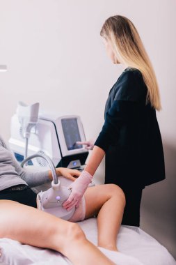 Beauty salon client, a woman getting a cryolipolysis procedure on her thigh to reduce fat by a beautician. clipart