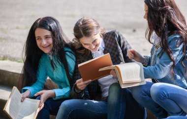 Üniversitenin bahçesinde elinde kitaplarla oturan bir grup kız öğrenci.