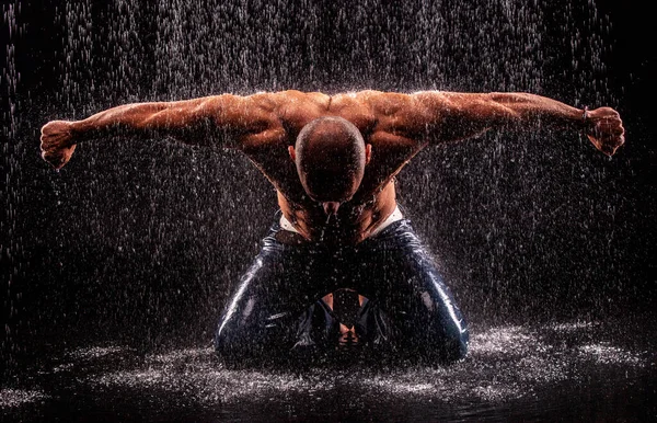 运动员健美运动员在黑色背景的雨柱下 — 图库照片