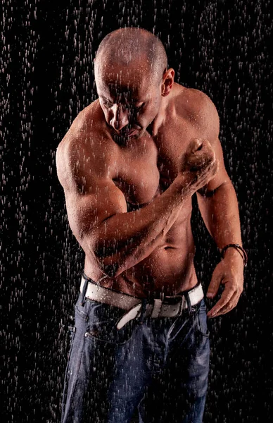 黒い背景に雨のジェットの下でアスリートのボディビルダー — ストック写真