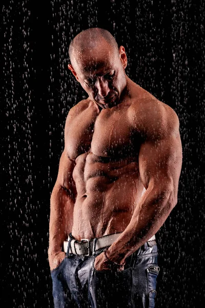 运动员健美运动员在黑色背景的雨柱下 — 图库照片