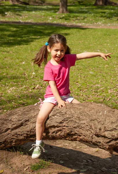 快乐的小女孩坐在公园的一棵树上 — 图库照片