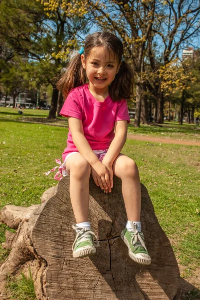 快乐的小女孩坐在公园的一棵树上 — 图库照片