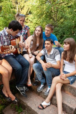 Bir grup genç, bir gitarla parkta dinleniyor.