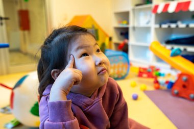 Genç kız oyuncaklarla dolu bir odada yerde oturuyor. Bir şeye bakıyor ve düşünüyor.