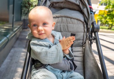 Bebek arabasında bir bebek oturuyor ve gülümsüyor. Bebek arabası gri ve siyah bir Han 'ı var.