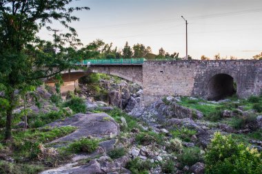 Yeşil trenin geçtiği bir nehrin üzerindeki köprü. Köprü taştan yapılmıştır ve tren yeşildir. Huzurlu ve huzurlu bir sahne.