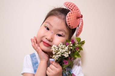 Elinde çiçek buketi tutan pembe bir saç bandı takan genç bir kız. Gözleri kapalı.