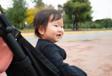 Bebek arabasında bir bebek oturuyor. Bebek arabası siyah ve siyah koltuğu var.