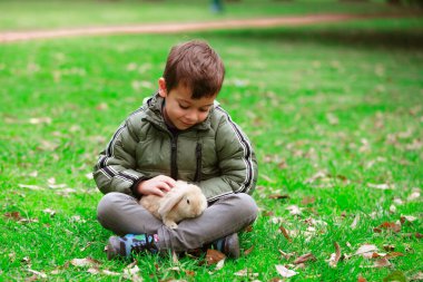 Kucağında bir tavşanla çimlerin üzerinde oturan bir çocuk. Tavşan küçük ve beyaz