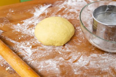 Mutfak masasında pizza hamuru topu. Tahta merdane ve un elek.