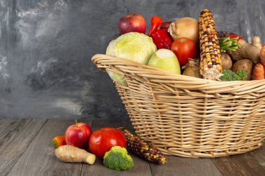 Sebze ve meyvelerle dolu sepet gri bir duvara yaslanmış. Metin için boşluk.