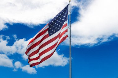 Rüzgarda dalgalanan büyük Amerikan bayrağı bulutlu mavi gökyüzüne karşı.