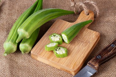 Kesme tahtasının üzerinde bıçakla kesilmiş bamya parçaları. Çuval bezinin arka planında.