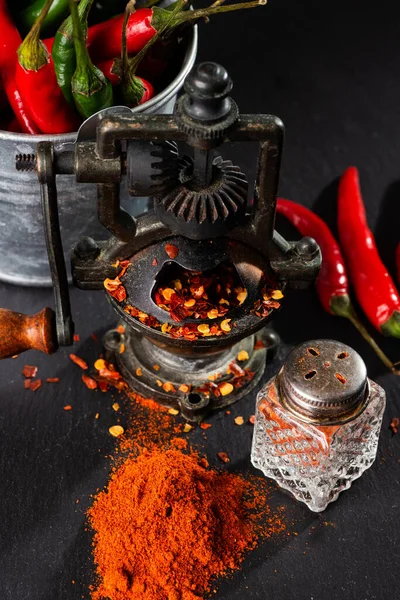 pepper mill, bunch of red peppers, capsicum and pepper pot on a black table. Close-up. Selective focus. Space for text.