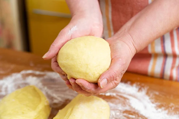 Female hands hold a ball of dough for bread. Flour and portions of dough are on the table. Close-up.
