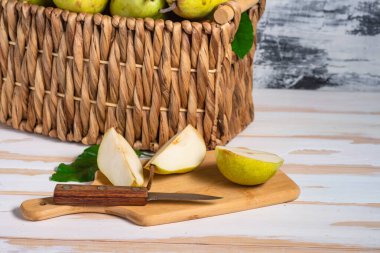 Hasır sepetteki taze armutlar ve kesme tahtasındaki armut dilimleri. Ev hasadı, taze toplanmış organik meyveler.