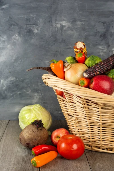 basket full of vegetables and fruits stands on the floor against a gray wall. Autumn and harvest time. Space for text.