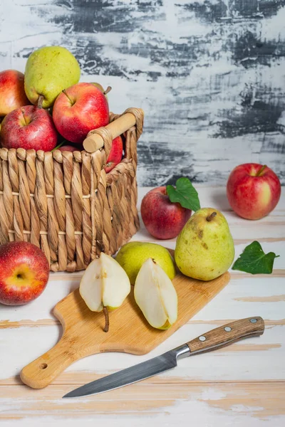 basket with pears and apples. Cutting board with pear slices and a knife.