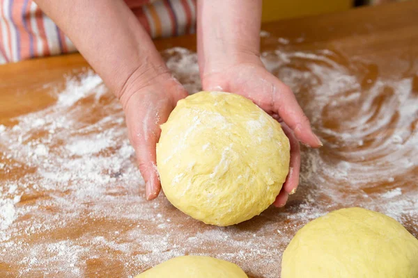 Female hands hold a ball of dough for bread. Flour and portions of dough are on the table. Close-up.