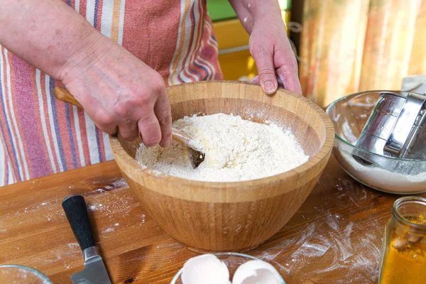 Close-up female hands knead the dough in a wooden bowl in the home kitchen.