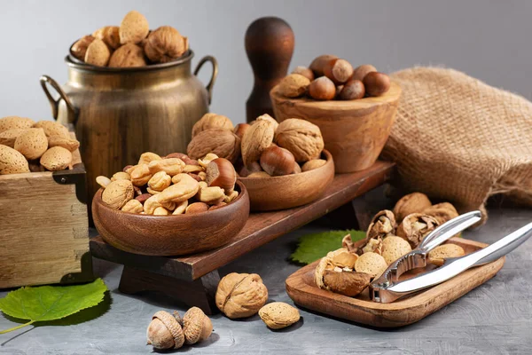 stock image nuts of different varieties in a wooden bowls and nut cracker on gray table. Close-up. selective focus.