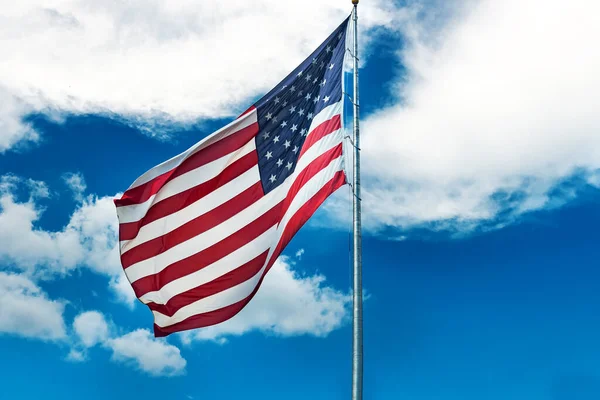 Large American flag waving in the wind against a cloudy blue sky. Low angle view of stars and stripes on american flag against blue sky