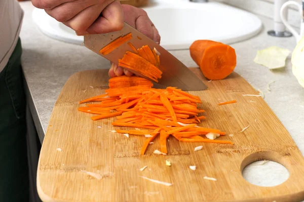 Stock image Chefs hands chopping carrot on wooden board. Cuts fresh carrots before cooking.