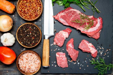 Organik çiğ et, sığır eti ya da kuzu eti koyu bir taş ya da beton arka planda. Sebze ve baharatlar. Kopyalama alanı olan üst görünüm.