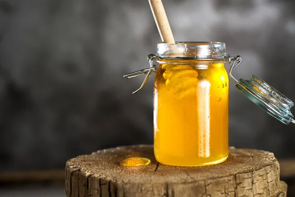 Stock image Fresh honey in a transparent jar on a wooden stump, on a gray background. Space for text.