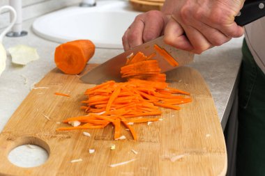 Kesme tahtasında havuç kesen bir kadının yakın çekimi.