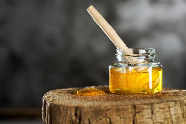 Gri bir arka planda, tahta bir kütükte şeffaf kavanozda taze bal. Metin için boşluk.