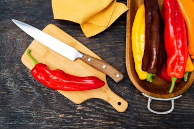 Kesme tahtasında bıçakla taze çiğ tatlı biber. Pişirmeye hazır. Koyu ahşap masa, üst manzara..