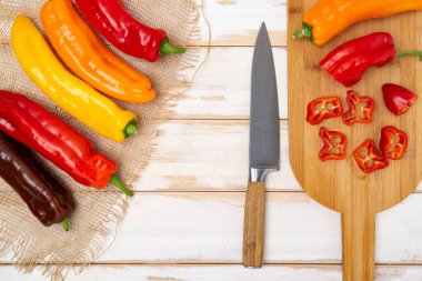 Kesme tahtasının üzerinde bıçakla taze tatlı biber. Doğranmış biber parçaları pişmeye hazır. Açık ahşap masa, üst manzara. Metin için boşluk.
