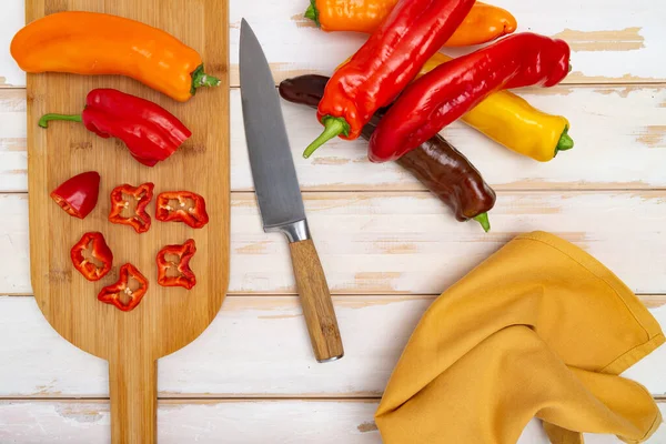 stock image Fresh sweet pepper (bell pepper) on a cutting board with a knife. Chopped pepper pieces are ready to cook. Light wooden table, top view. 