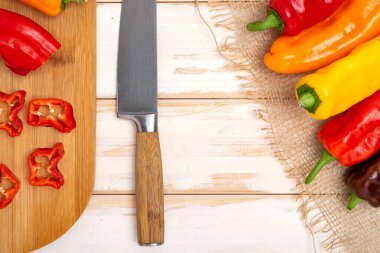 Kesme tahtasının üzerinde bıçakla taze tatlı biber. Doğranmış biber parçaları pişmeye hazır. Açık ahşap masa, üst manzara. Metin için boşluk.