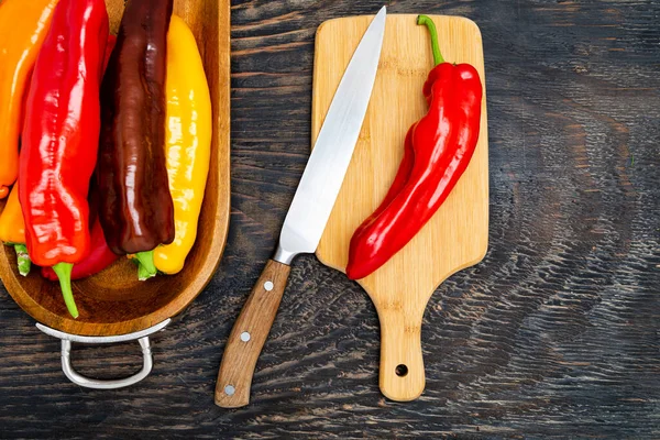 stock image Fresh raw sweet pepper (bell pepper) on a cutting board with a knife. Ready to cook. Dark wooden table, top view.