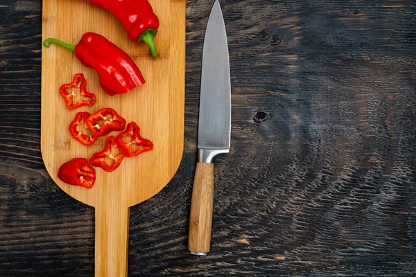 stock image Fresh raw sweet pepper (bell pepper) on a cutting board with a knife. Chopped pepper pieces are ready to cook. Dark wooden table, top view.Space for text.